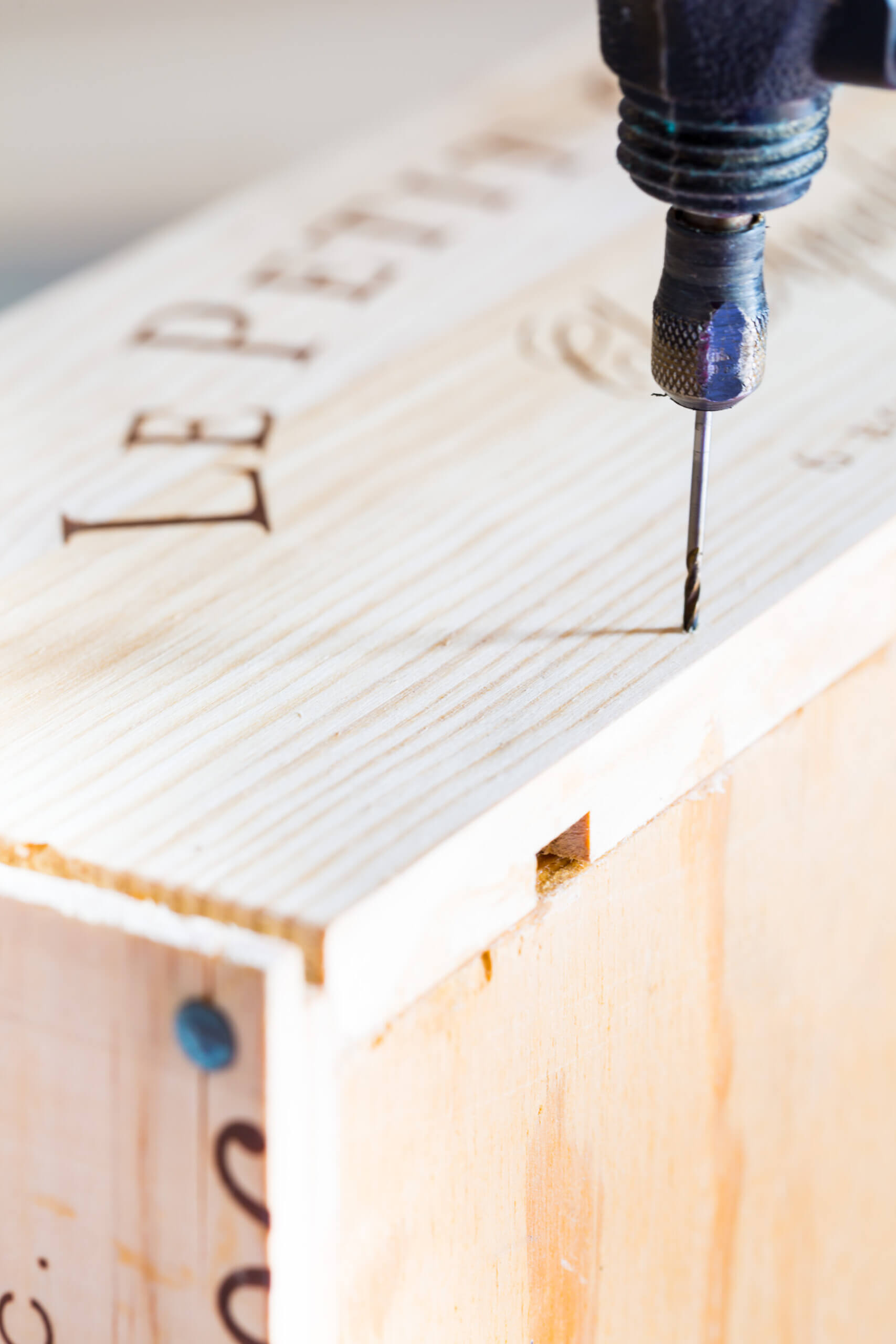 Drilling a hole for a nail in the side of a recipe box made using a wooden wine crate.
