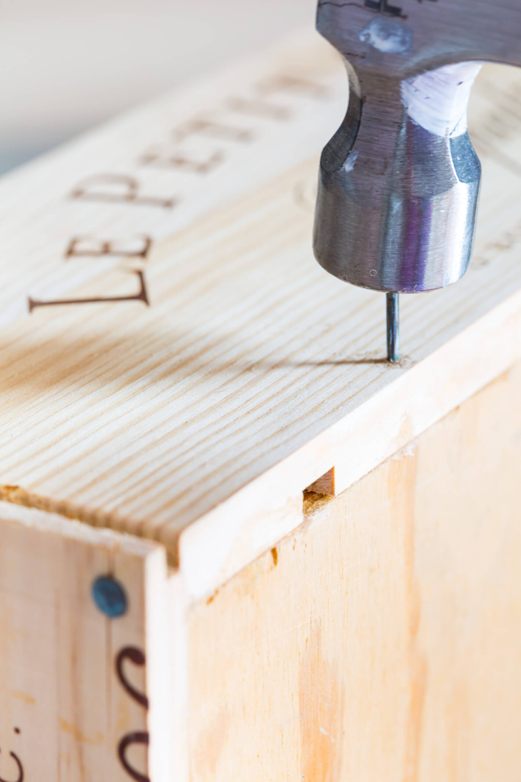 Hammering in a nail to make a diy recipe card box using wine crate panels.