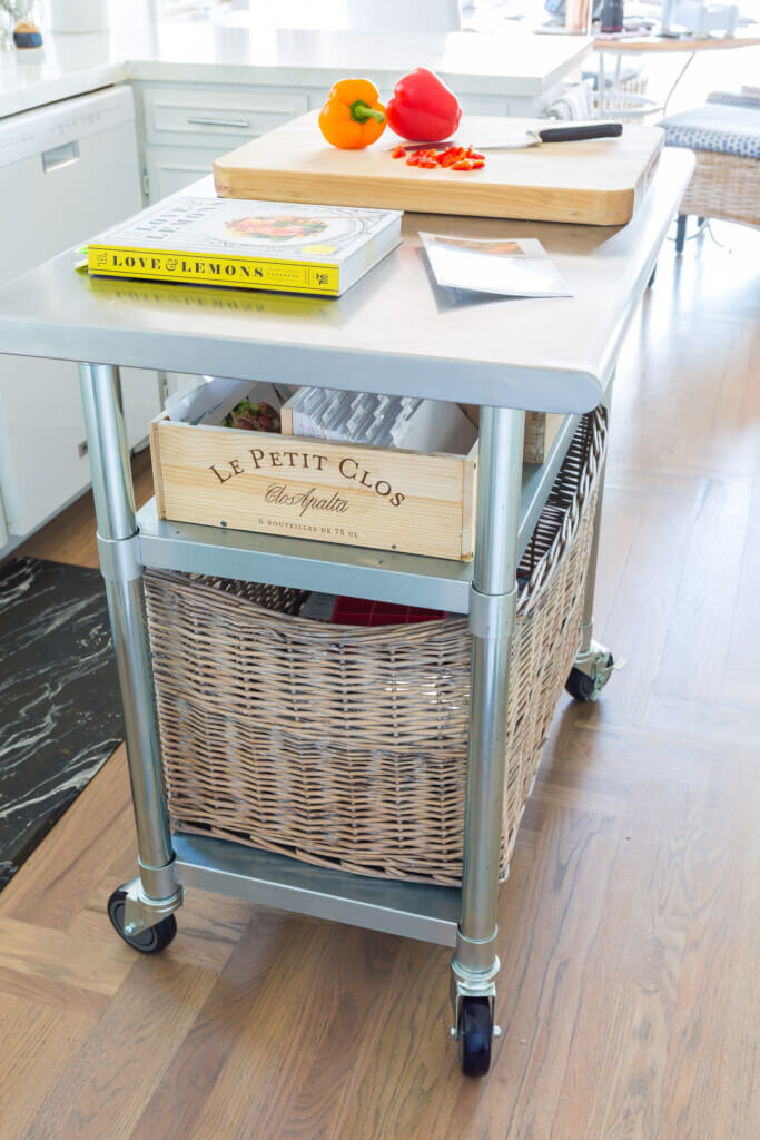 A metal kitchen cart turned into an island for food prep. It holds a repurposed wine crate that was turned into a recipe card holder.