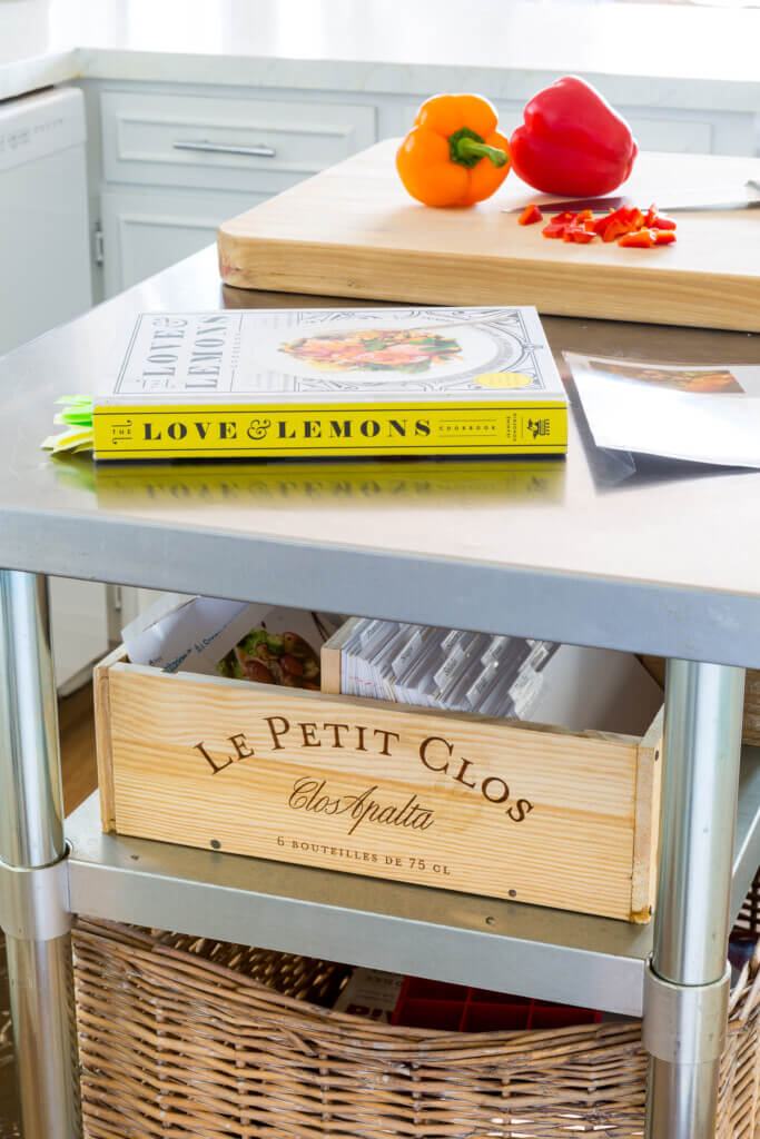Kitchen island card with cookbook on top and cutting board on top. A wine box repurposed into a recipe box on second shelf. Makes it easier to eat a plant-based diet.