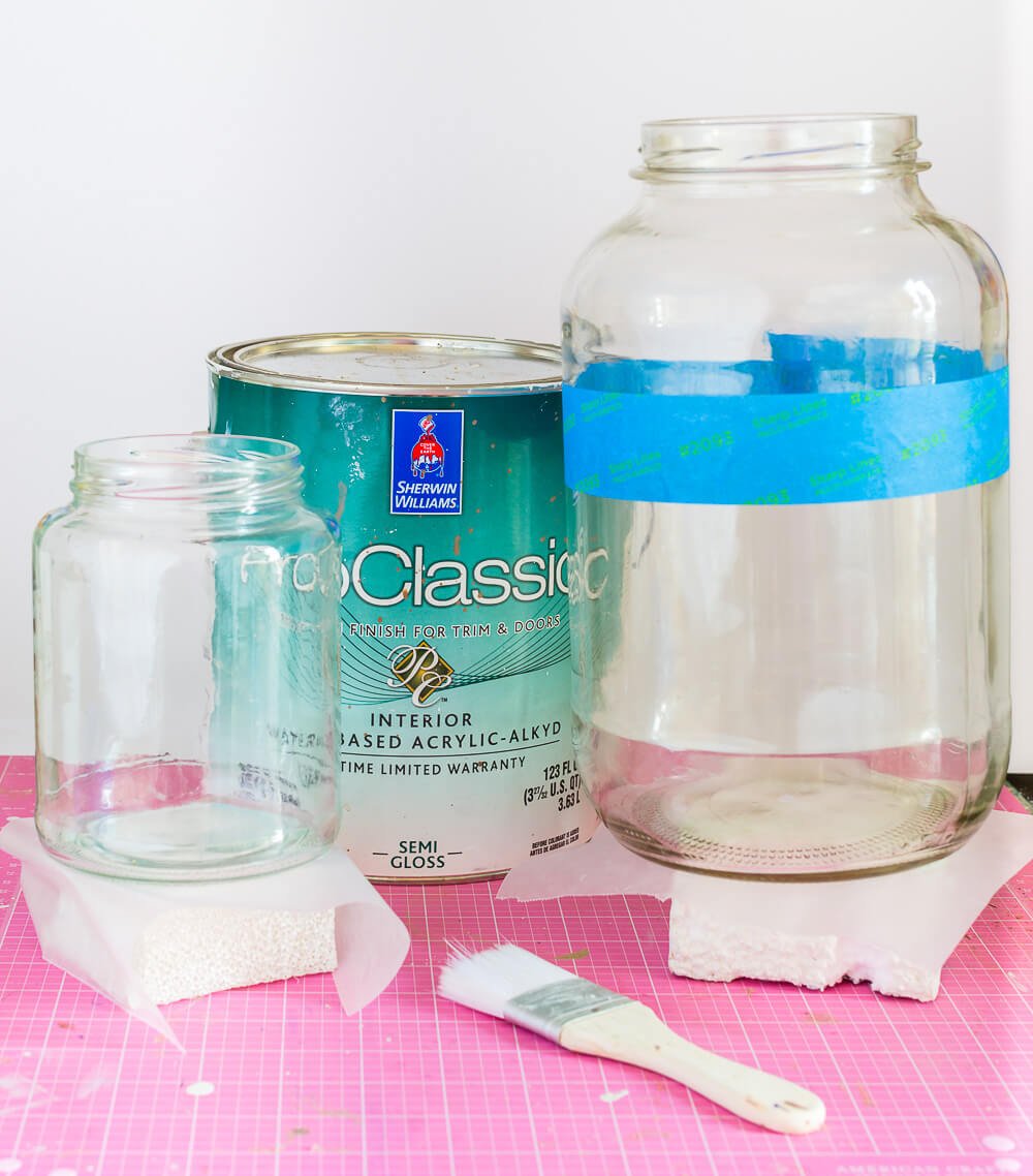 Two sizes of glass pickle jars getting prepared to dip into paint to create modern looking dipped vases.