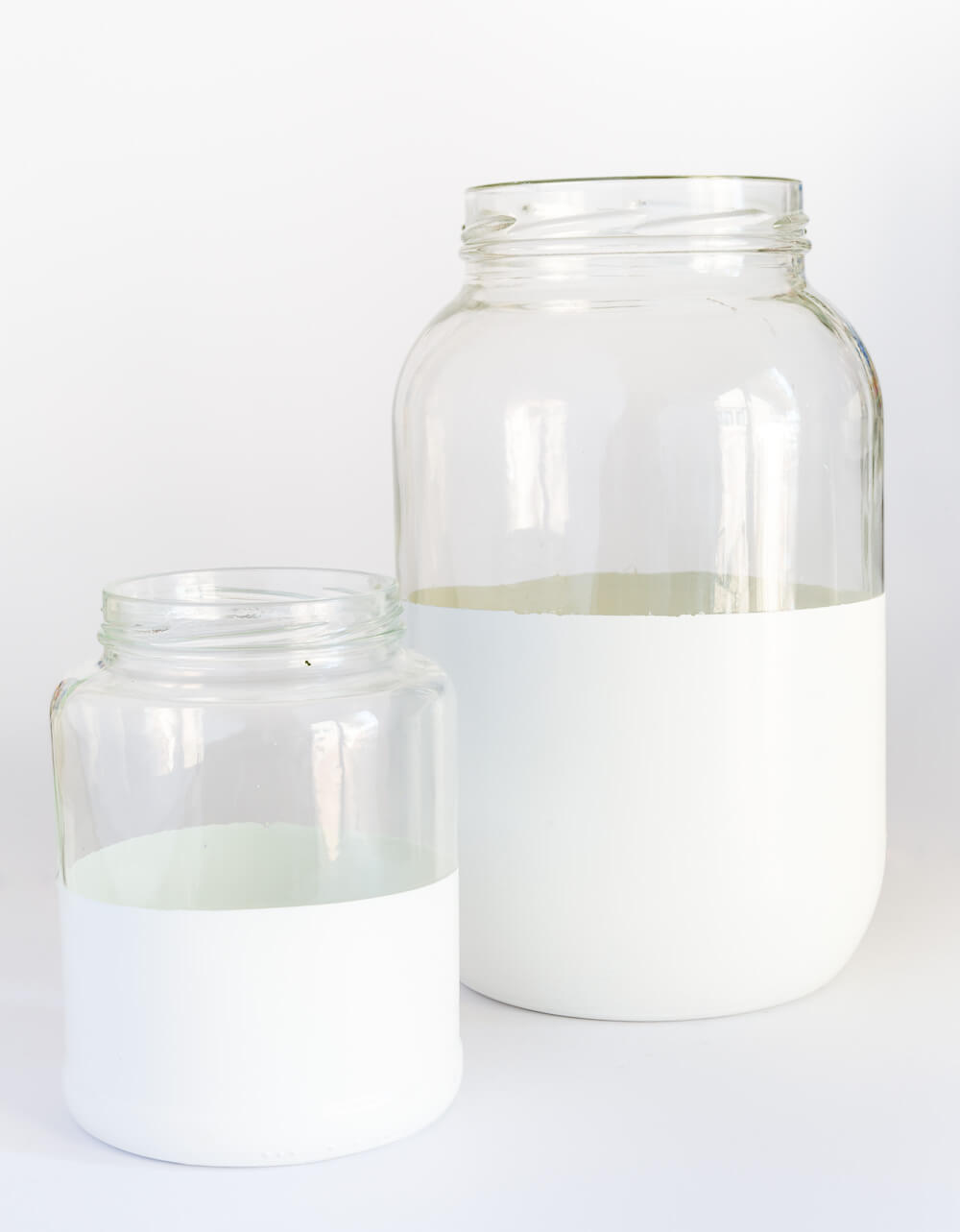 Two glass pickle jars after getting dipped or painted with white paint. They now look like trendy decor vases like the high end decorating catalogs sell.