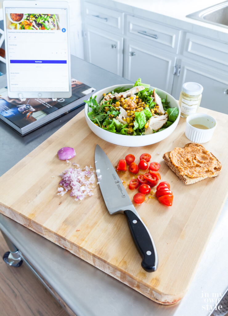 Food being chopped on a cutting board on a metal cart kitchen island.