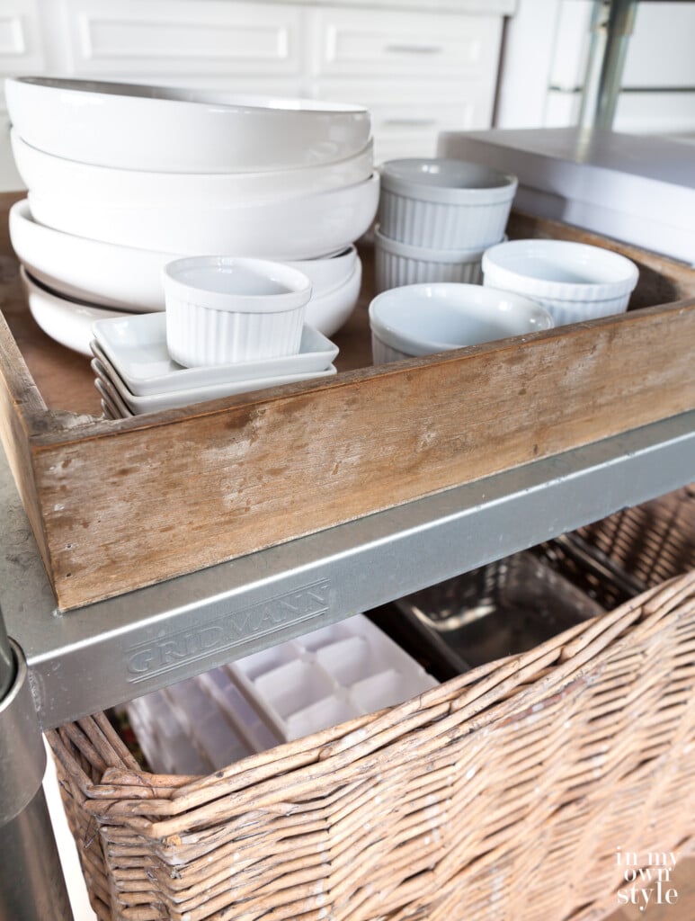 White plates, bowls and ramekins in a wood box on kitchen cart island.