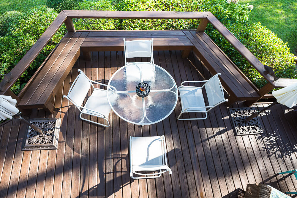 Looking down from second floor to round white outdoor table and chairs on stained wood deck.