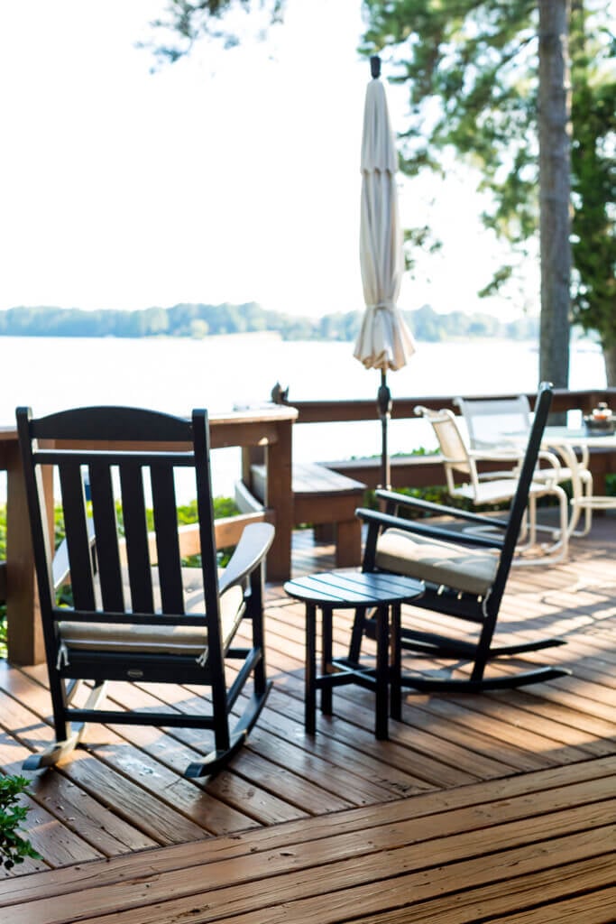 Two black outdoor rockers on deck over looking a lake.