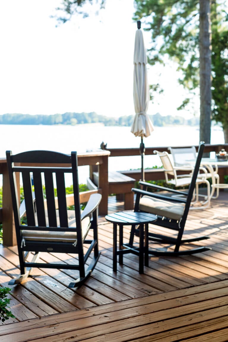 Two black outdoor rockers on deck over looking a lake.