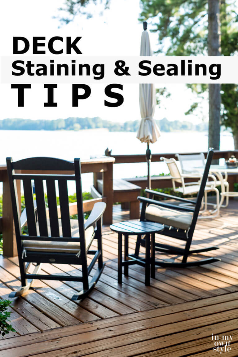 Two black outdoor rockers on lakeside deck. Text overlay says Deck Staining and Sealing Tips