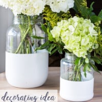 Two glass pickle jars transformed into chic vases by dipping in white paint. Text overlay says Decorating Idea using pickle jars.