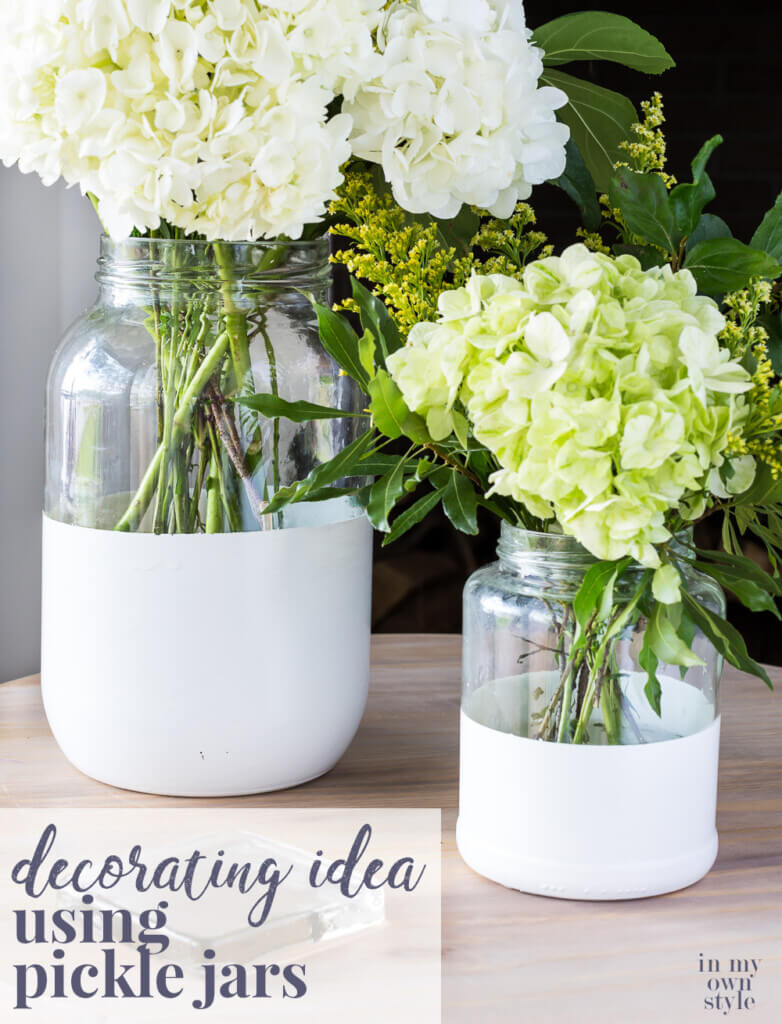 Two glass pickle jars transformed into chic vases by dipping in white paint. Text overlay says Decorating Idea using pickle jars.