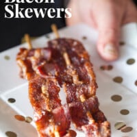 Sweet and spicy bacon on skewers on a white plate with gold dots. Text overlay says Sweet & Spicy Bacon Skewers