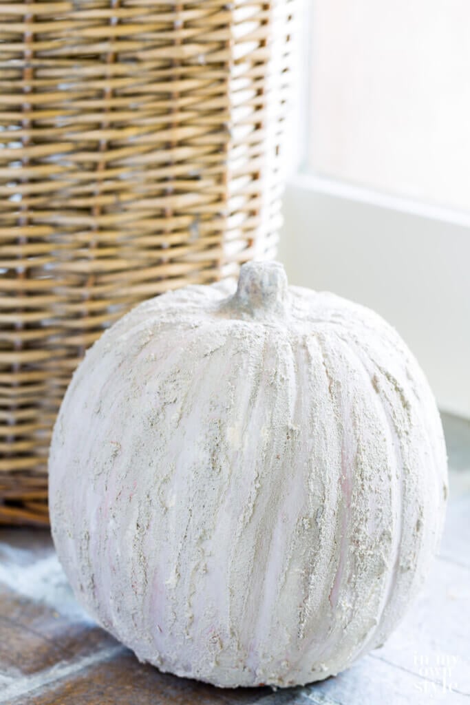 Tall handled basket with stone pumpkin in front of it.