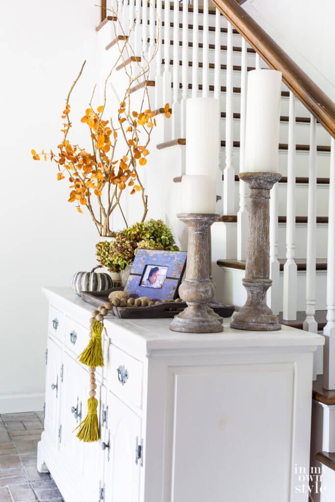 Sideboard in entryway of house decorated for fall using various heights of decor.