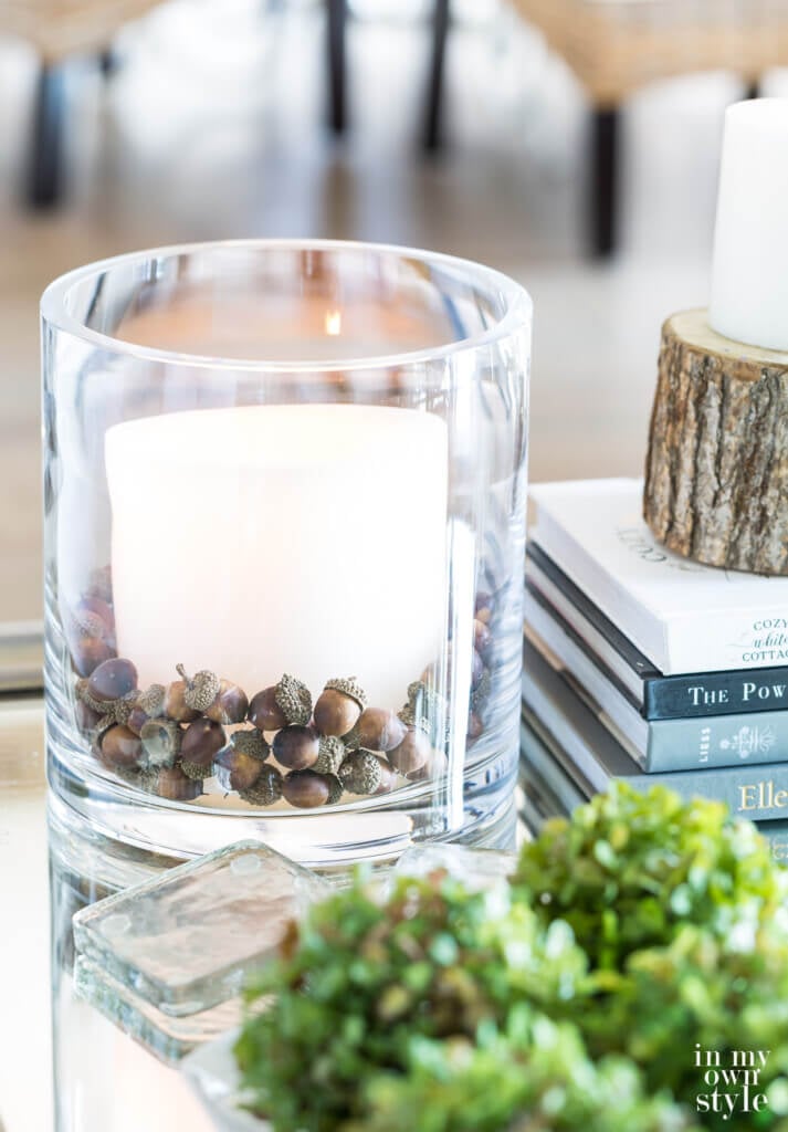 Pottery Barn glass cylinder vase filled with acorns and large white candle on a coffee table.
