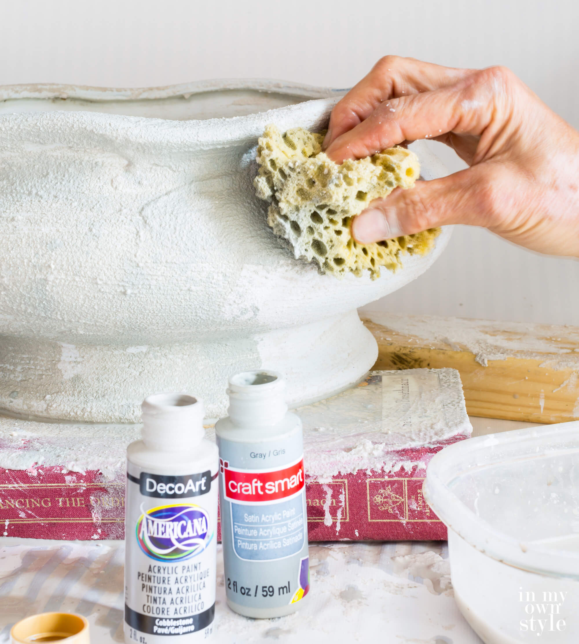 Using a sea sponge to apply paint over texture layer of stucco patch on large bowl planter.