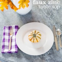 Looking down on faux painted to look like zinc table. Place setting and fall flowers on table. Text overlay sys dit faux zinc table top