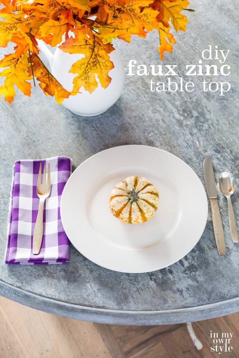 Looking down on faux painted to look like zinc table. Place setting and fall flowers on table. Text overlay sys dit faux zinc table top