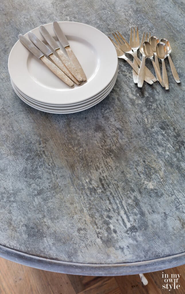 Faux zinc painted table with stack of white plates and silverware