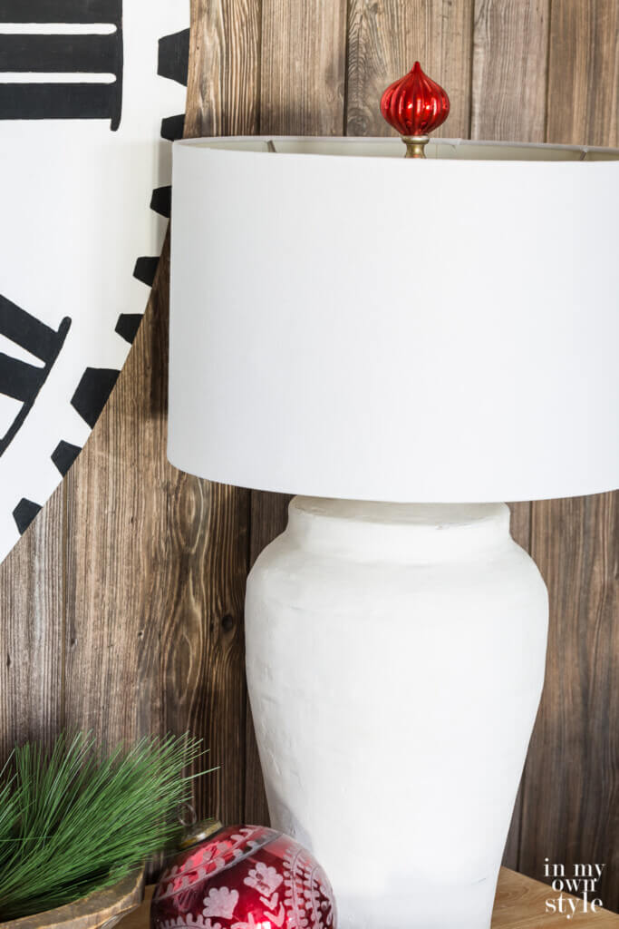Holiday lamp finial idea. Close up of white table lamp with red Christmas ball ornament made into a finial above the lamp shade.