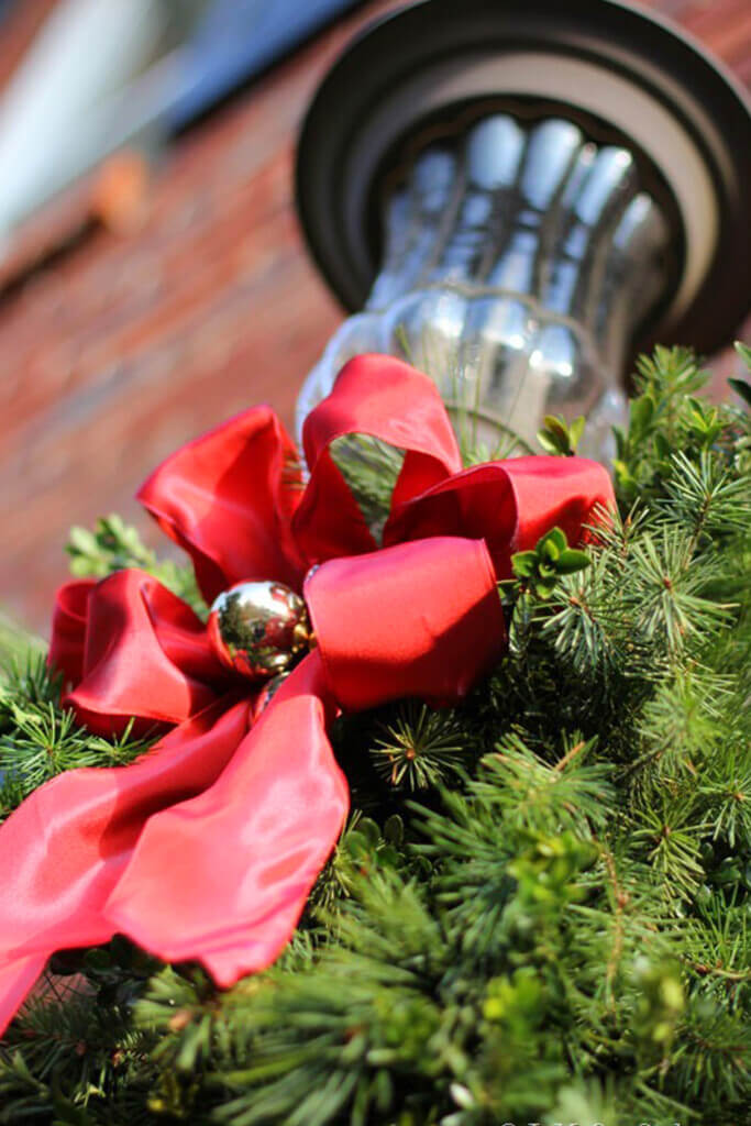 Outdoor light fixture on house with a red bow and greenery.