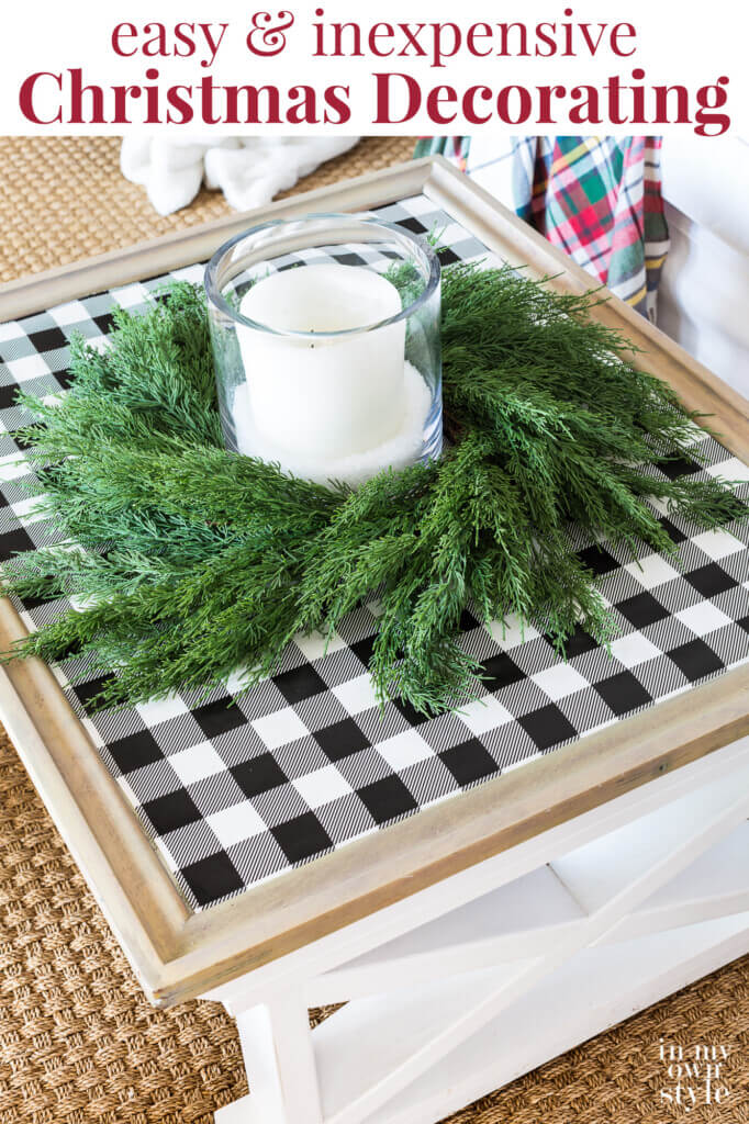 Farmhouse coffee table decorated for Christmas with black and white checked gift wrap on table top with cedar wreath and candle. Text overlay say easy and inexpensive Christmas decorating.