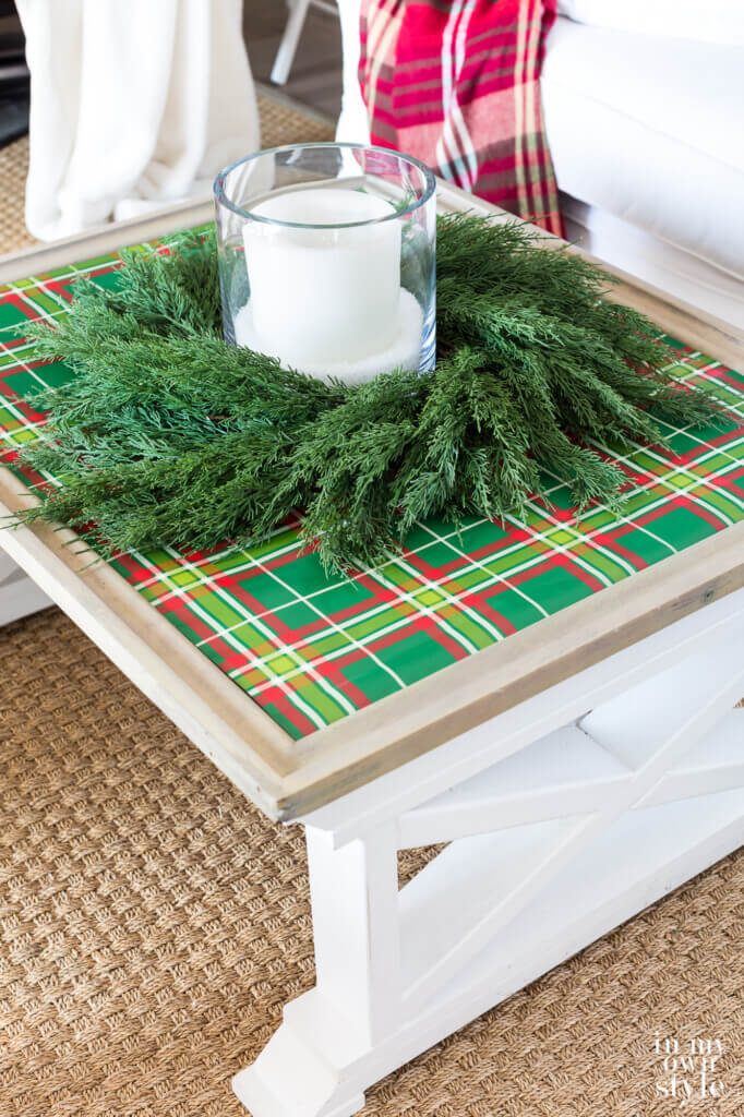 Coffee table covered with green plaid gift wrap, wreath and candle.
