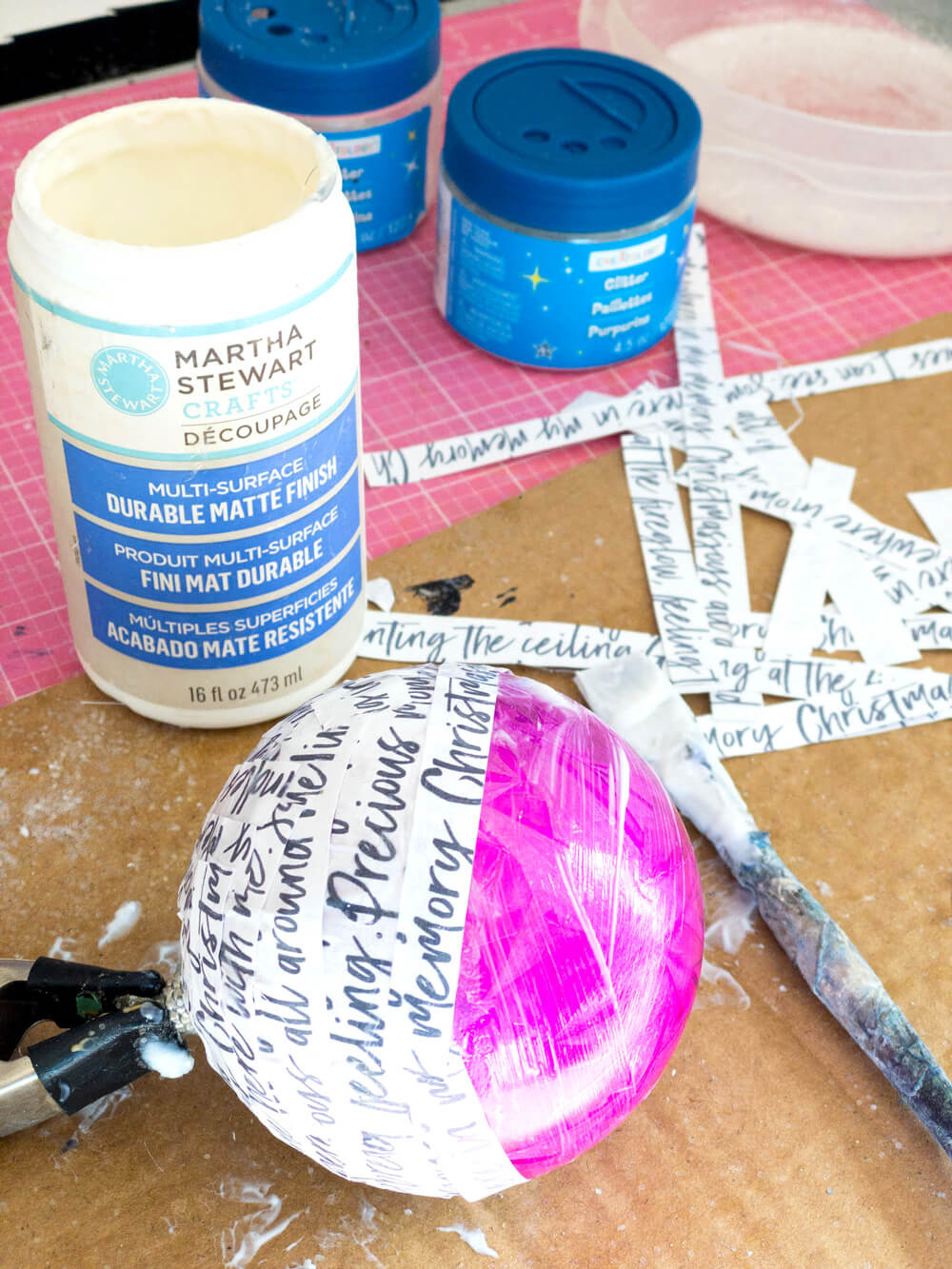 glueing strips of hand script paper to Christmas ornaments.