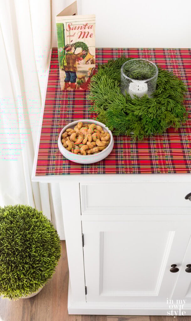 Plaid giftwrap covering the top of a sideboard is one affordable Christmas decorating idea.