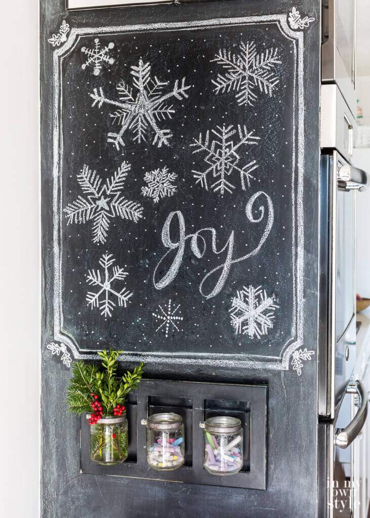 Wall Chalkboard in kitchen with snowflakes and the word Joy drawn on.