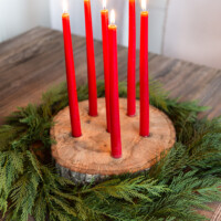 Tree trunk slice taper candle holder for Christmas with cedar branches around it.