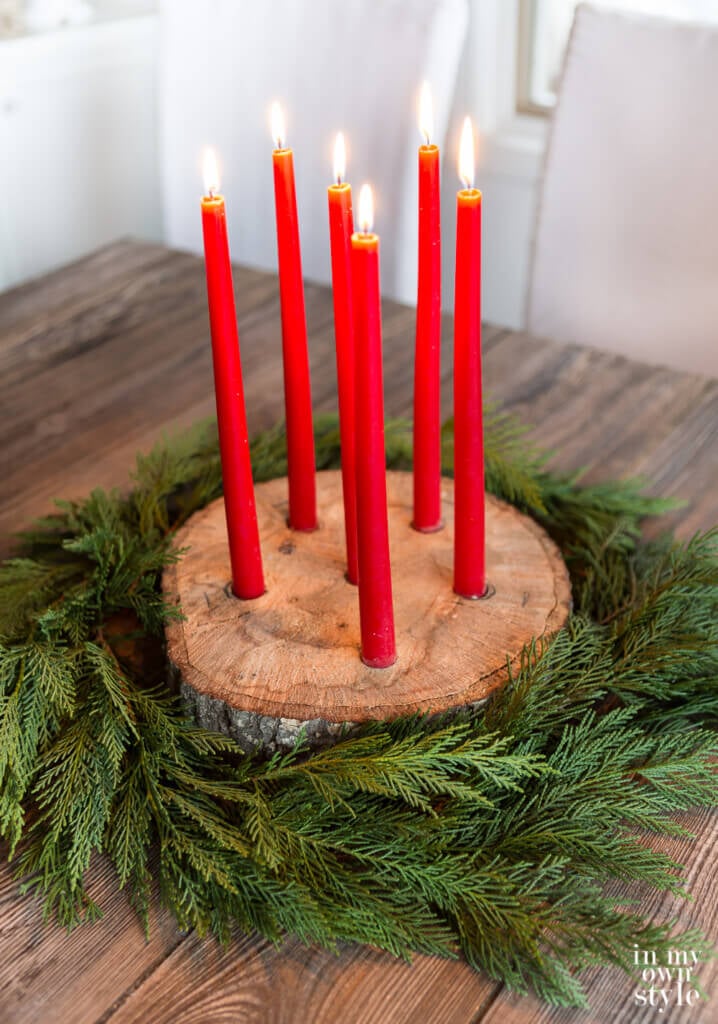 Tree trunk slice taper candle holder for Christmas with cedar branches around it.