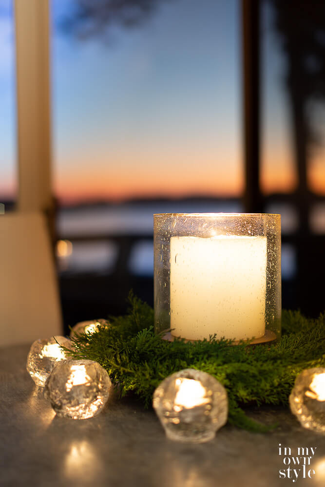 Large candle in seeded glass hurricane on kitchen table with smaller candles around it to provide cozy light.