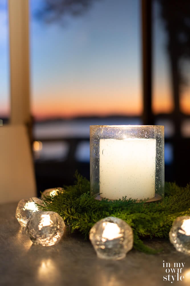 Large candle in seeded glass hurricane on kitchen table with smaller candles around it to provide cozy light.