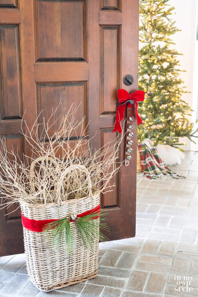 Red ribbon around large basket filled with branches. Christmas tree in distance.