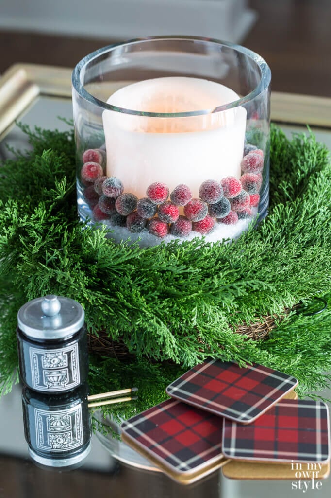 White candle with cranberries around it sitting on a cedar wreath on living room coffee table decorated for Christmas