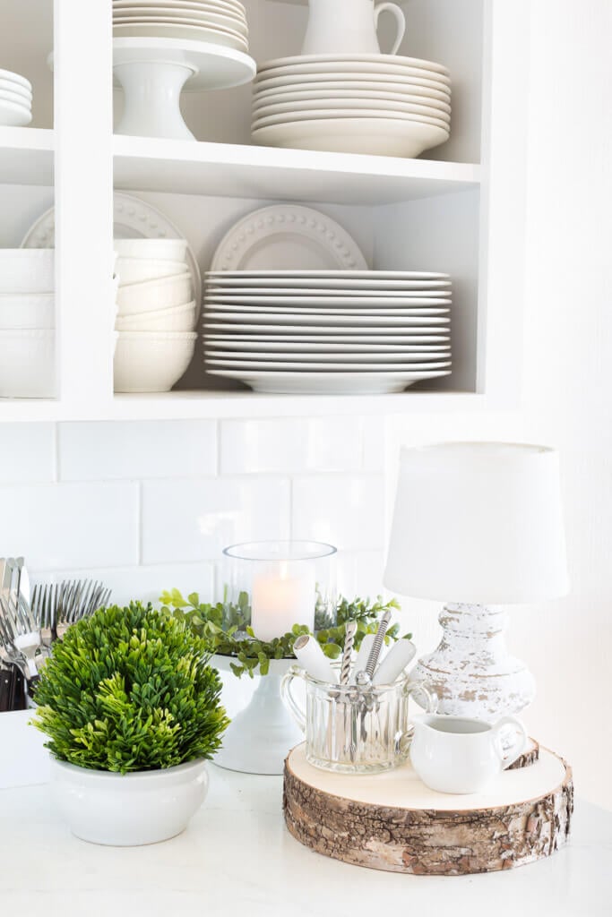 After Christmas decorating ideas for the kitchen. White kitchen with greenery and white plates and dishes on a counter.