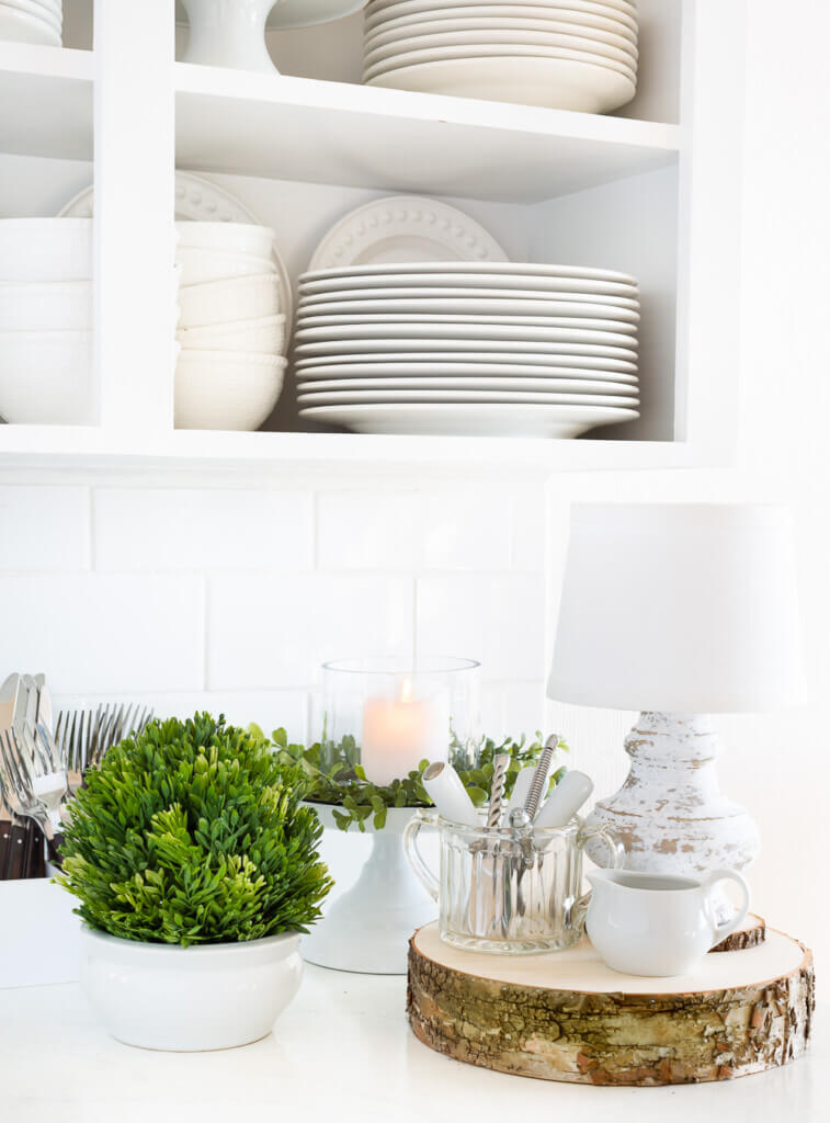 After Christmas decorating ideas for the kitchen. White kitchen with greenery and white plates and dishes on a counter.