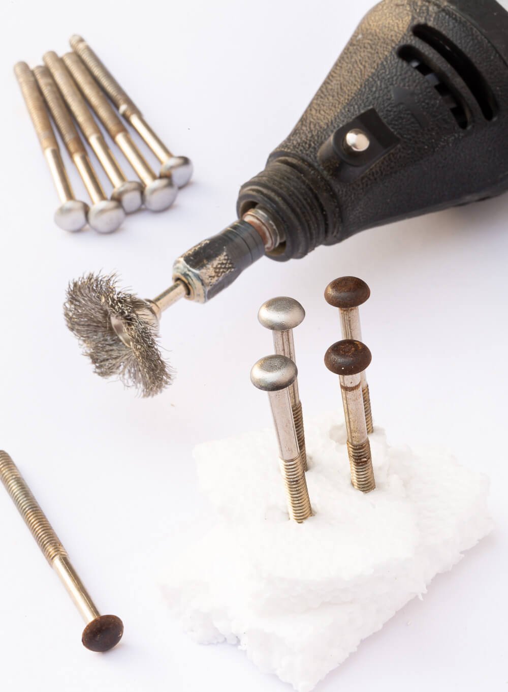 Dremel Mulit-Use tool wire brush to remove aged rust on drawer knob screws.