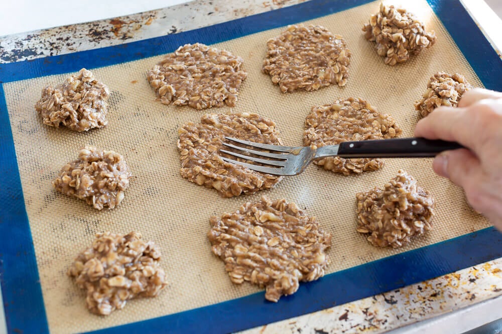 Flattening banana oatmeal cookies on baking sheet with a fork