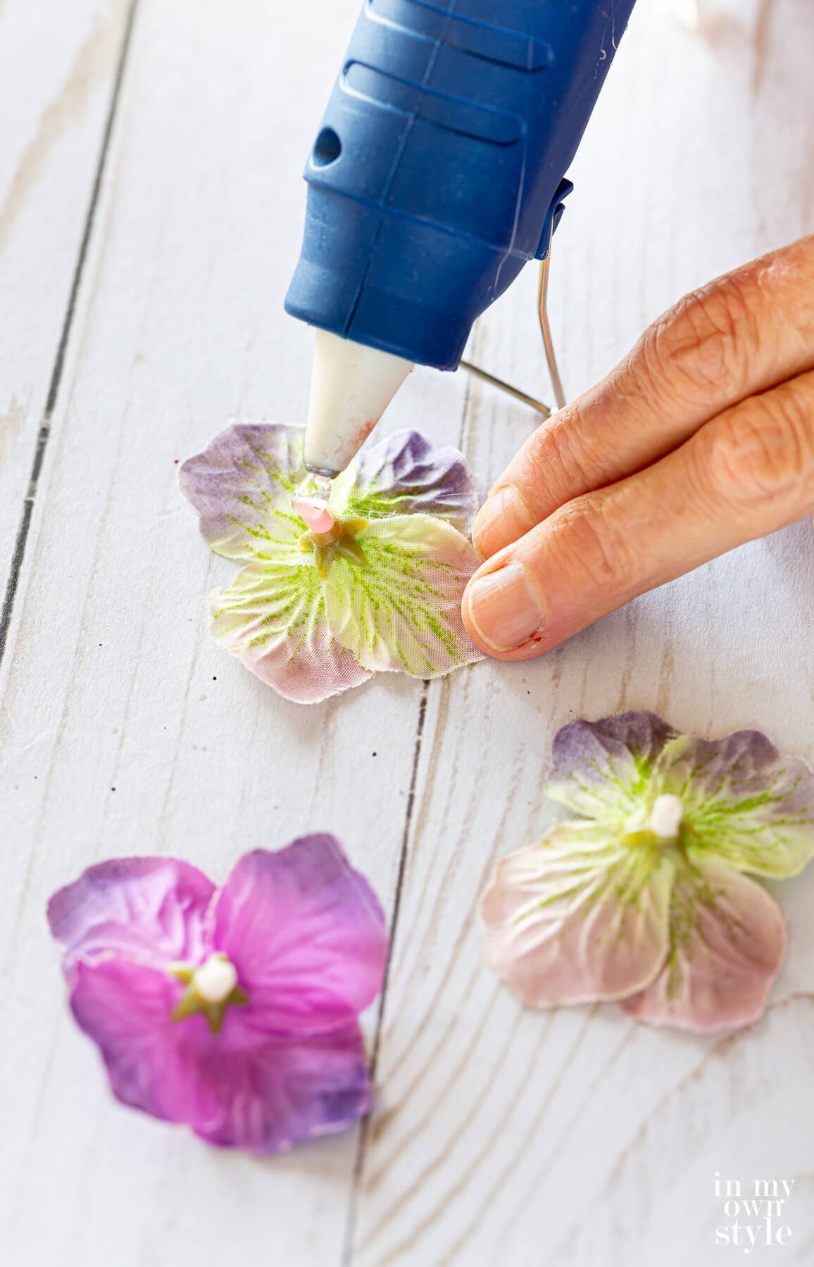 Adding hot glue to the back of snipped purple flower blooms from a fake flower stem.