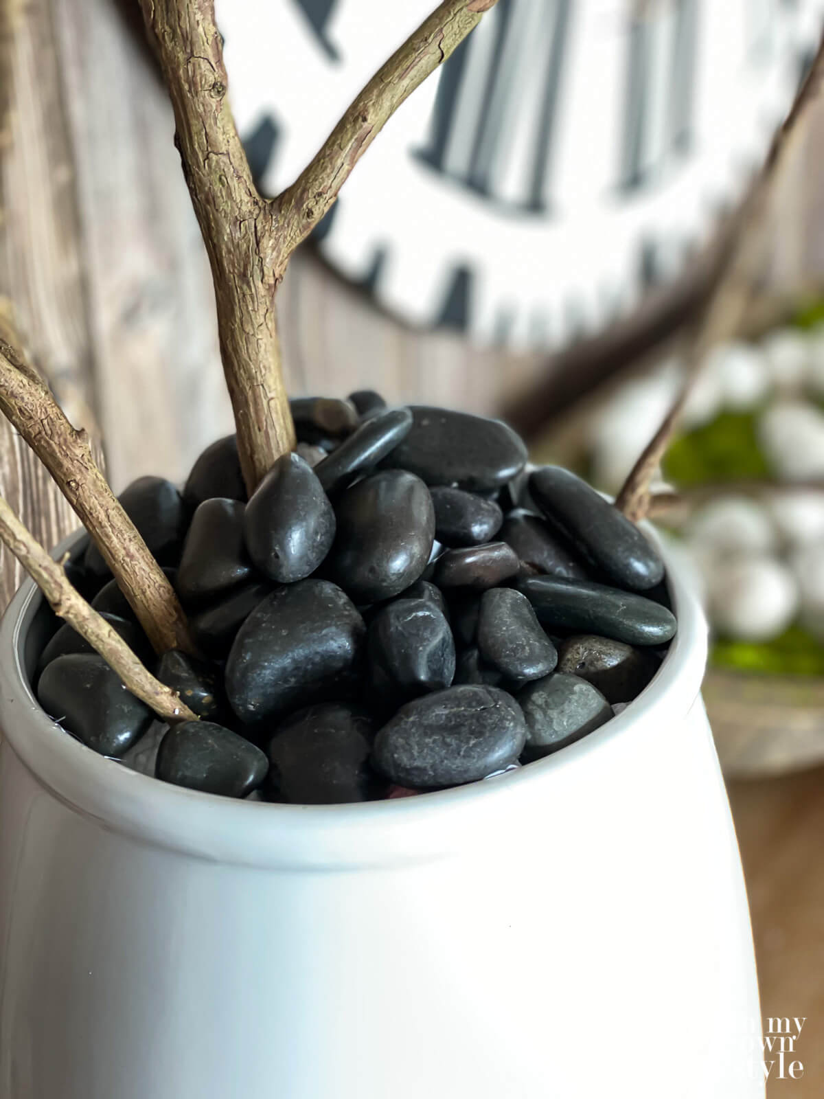 Black river rocks used instead of moss in a ceramic planter filled with Faux blooming branches.