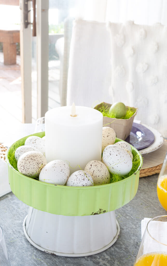 Easter brunch table centerpiece. Metal two-tiered stand filled with speckled eggs and a white candle.