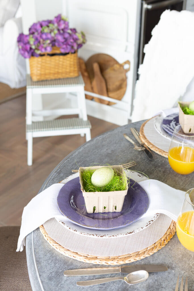 Side view of Easter brunch dining table in kitchen. In the background are Easter flowers and a white plates and wood cutting boards.