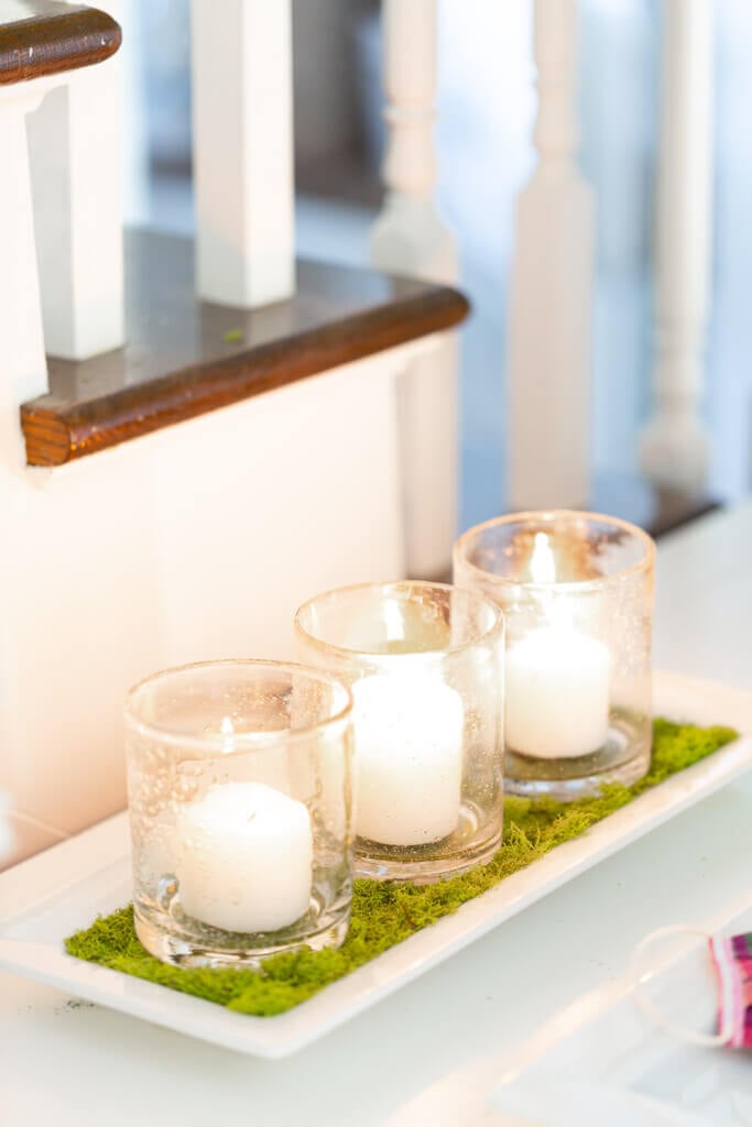 3 white candles on white moss lined tray.