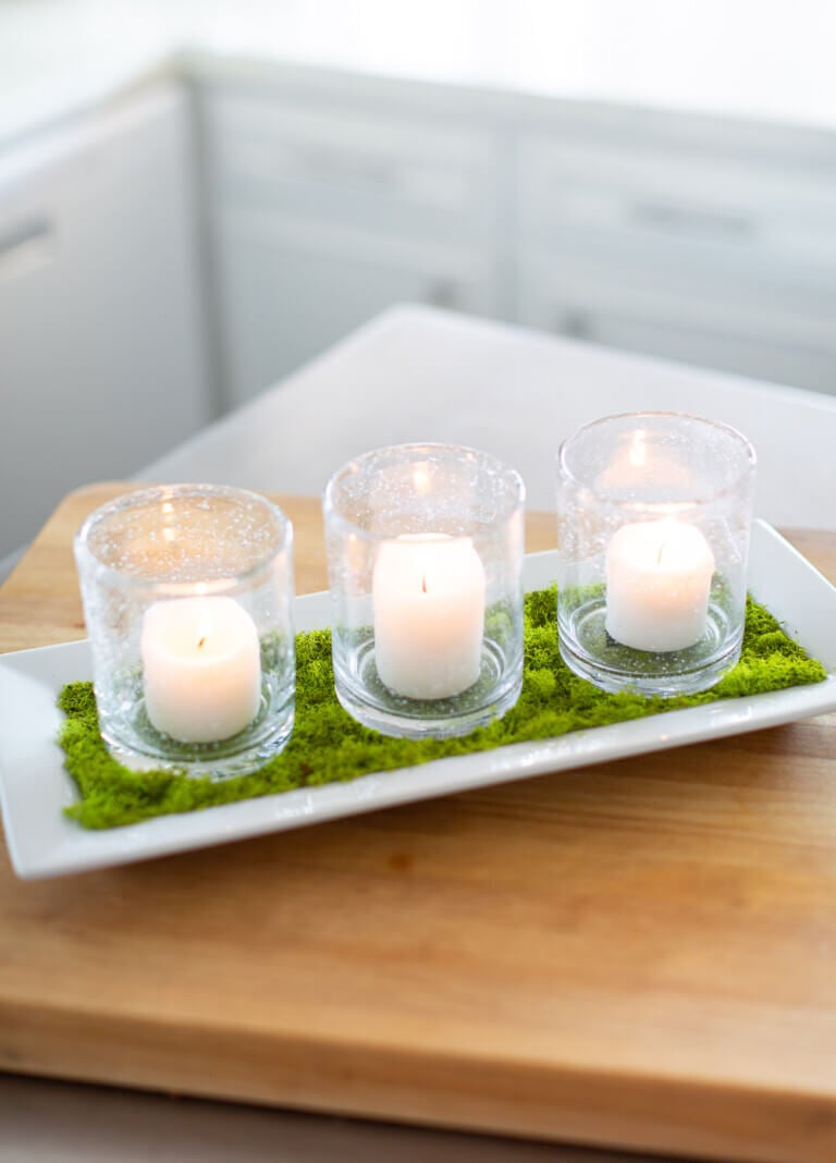 Spring candle decoration for console table DIY made using 3 candles in drinking glasses on a moss covered tray.