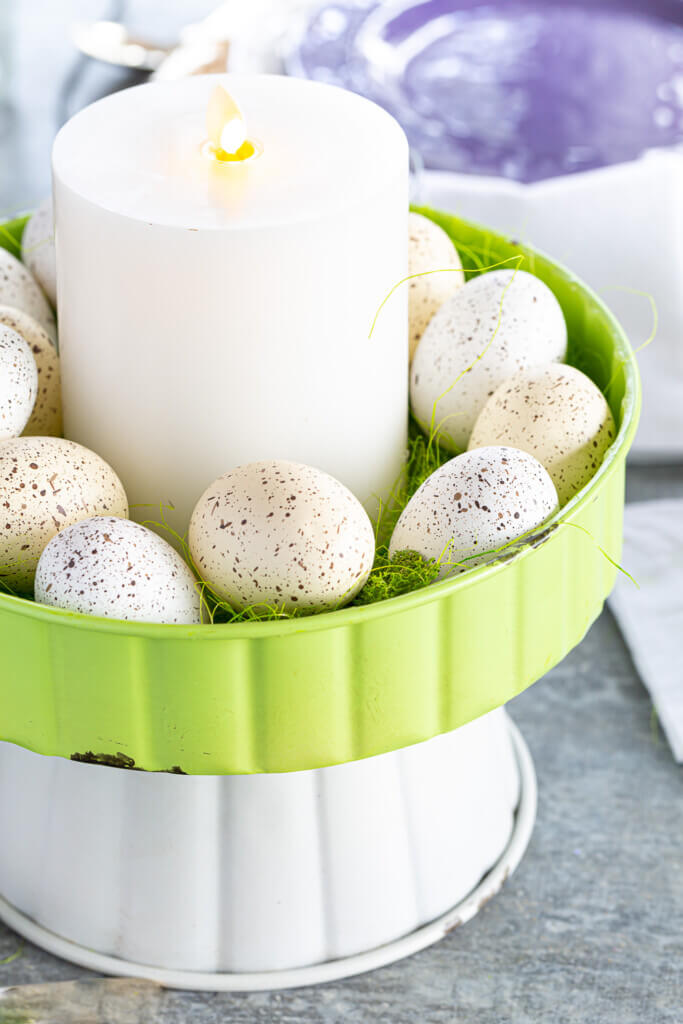 Easter brunch table centerpiece idea using a metal pedestal, speckled eggs and a white candle.