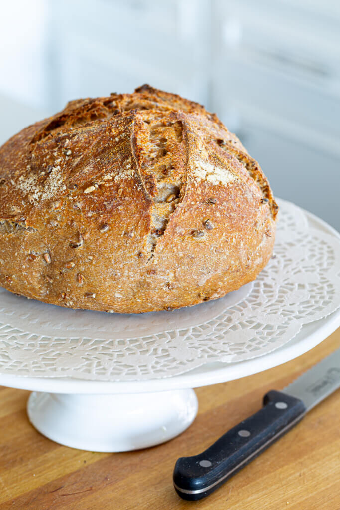 A loaf of sourdough bread on a white cake stand.