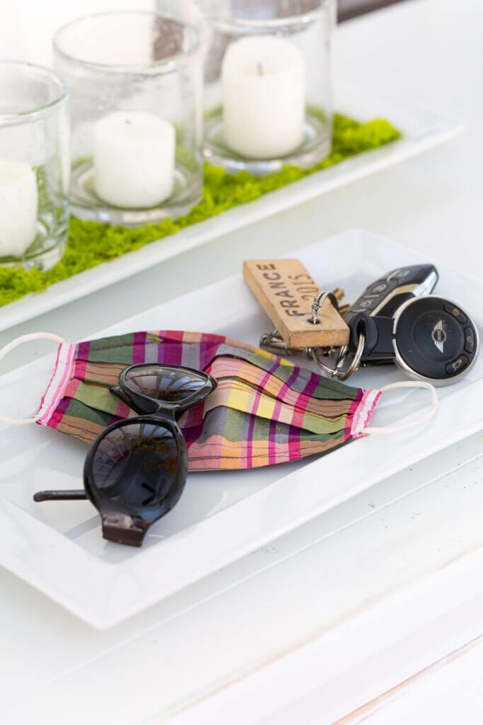 White ceramic tray on console table that holds sunglasses, keys and a plaid face mask.