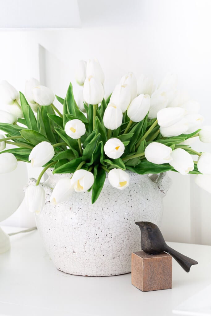 White tulips in white crackle finish cachepot. Black bird on wood cube. Both on a foyer console table.