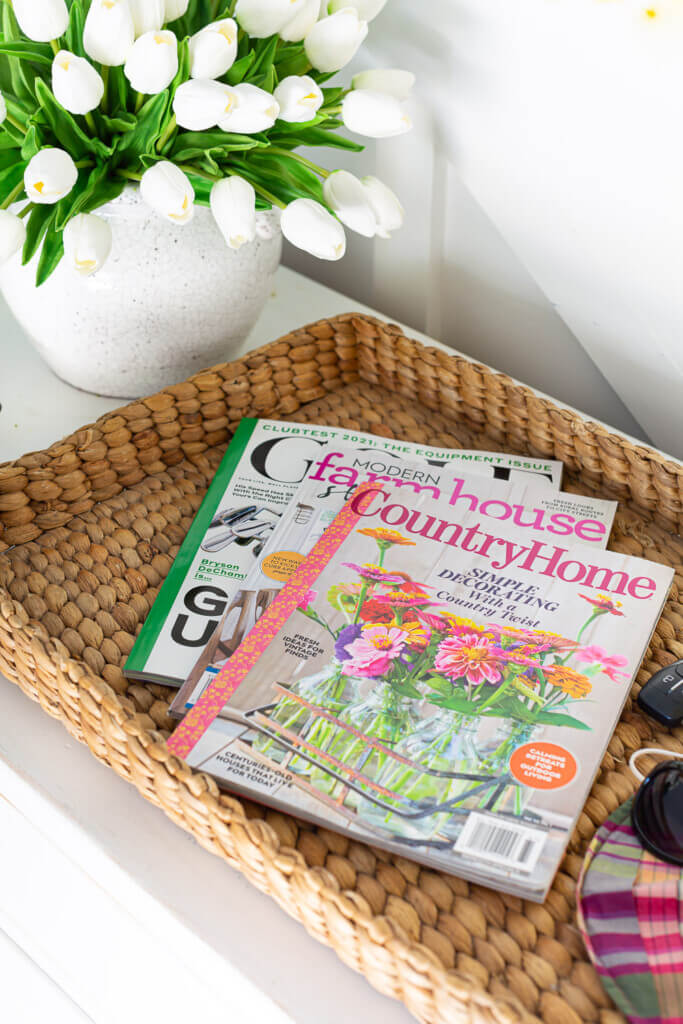 low sided woven basket with 3 decorating magazines in it. Placed on a console table.